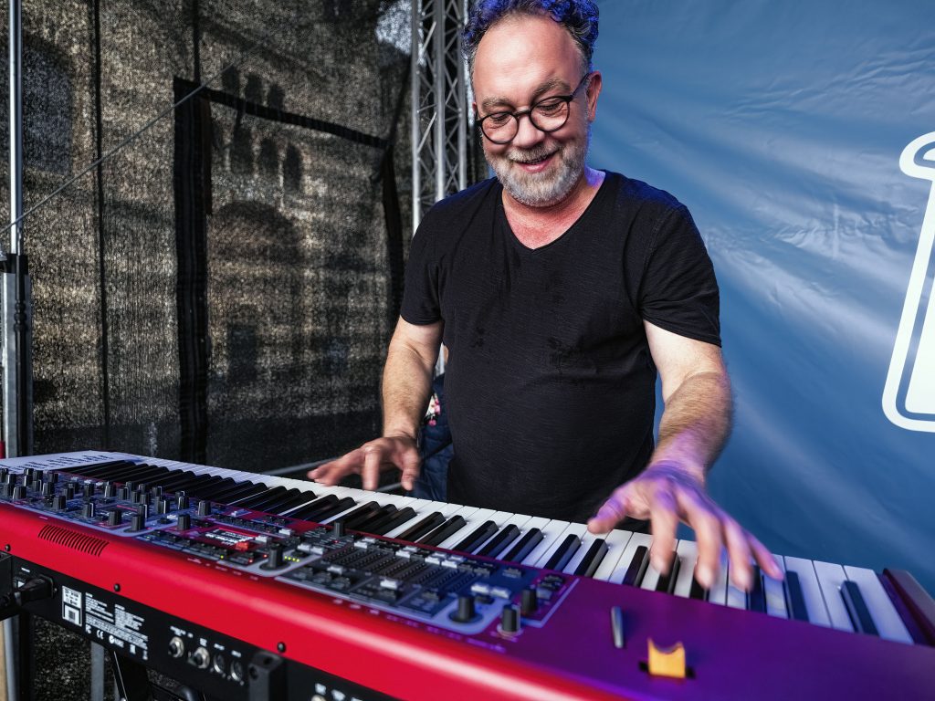 Lusthansa Mitglied mit einem schwarzen Shirt und Brille spielt Keyboard auf einer Bühne